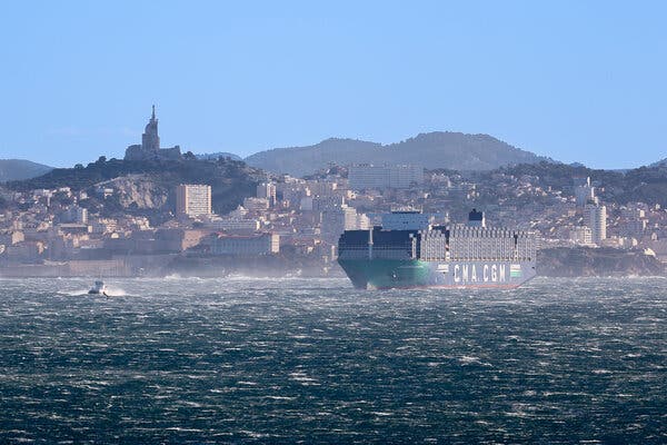 Loď s kontajnermi naskladanými vysoko na hlavnej palube. Za ním mesto Marseille vo Francúzsku.