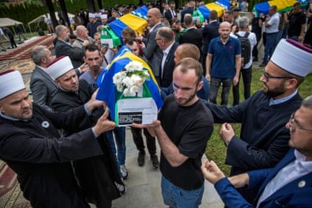Men carry coffins wrapped in the blue and yellow Bosnian flag.